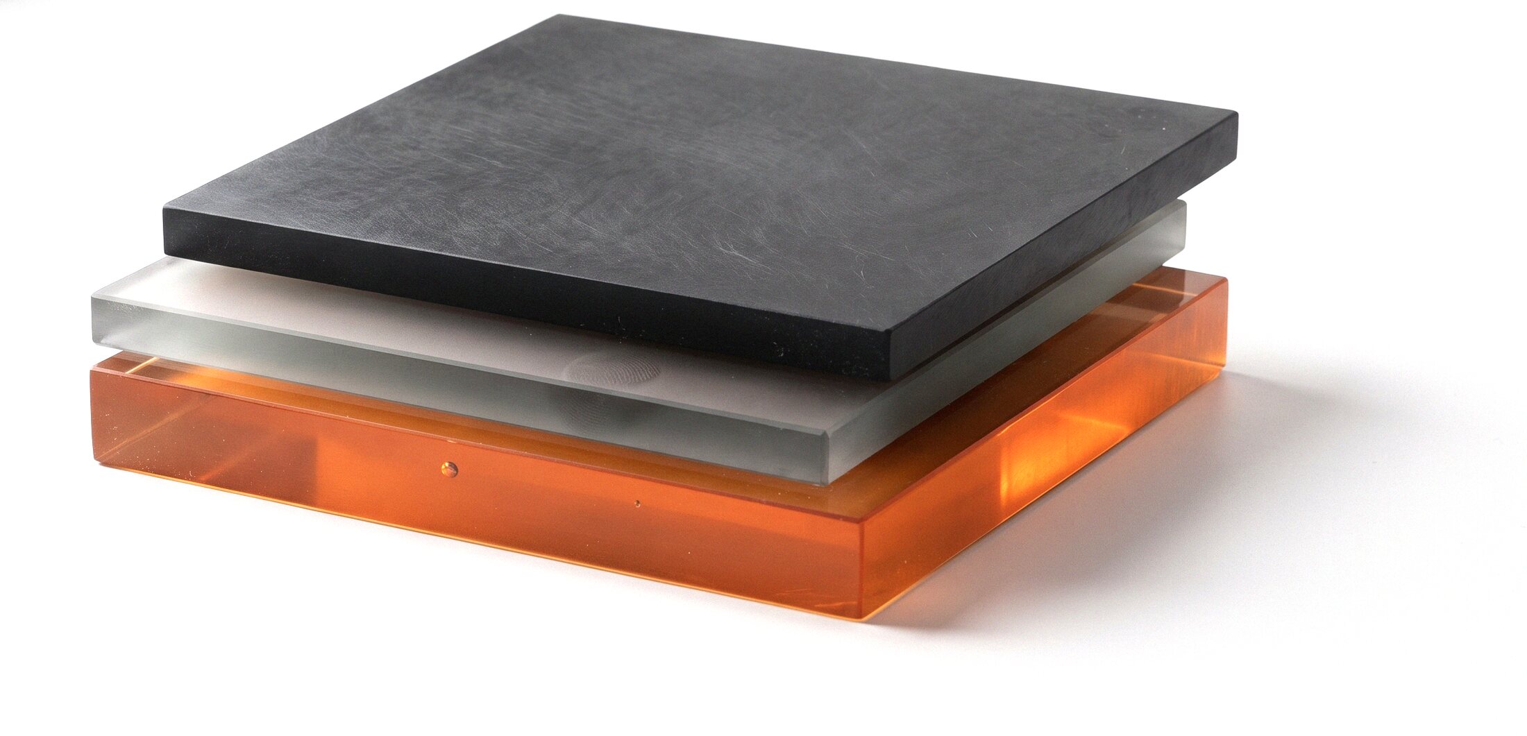 Three stacked slabs on white — matte black resin, frosted grey glass, and translucent iron-orange acrylic — the three horizons of a podzol soil.